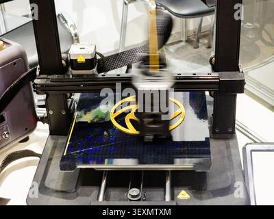 A close-up view of a modern FDM 3D printer in operation, extruding yellow plastic filament to manufacture a circular prototype part with motion blur o Stock Photo