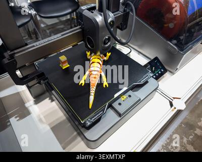 A close-up shot of a modern desktop 3D printer in action, fabricating a vibrant, multi-colored articulated toy lizard on its heated build plate. Stock Photo