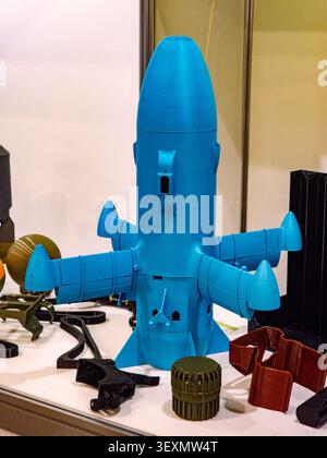 A bright blue 3D-printed plastic model of a rocket or missile prototype displayed on a table alongside other industrial and technical 3D printed compo Stock Photo