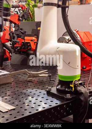 A white industrial collaborative robot (cobot) mounted on a modular perforated metal welding table in a modern manufacturing facility or exhibition. Stock Photo