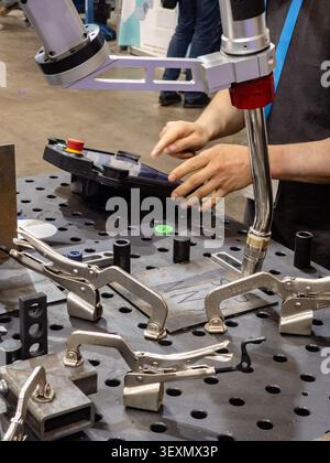 An industrial technician programs a collaborative robotic welder using a touch screen control panel, with metal locking clamps securing the workpiece Stock Photo