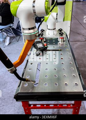 A high-tech collaborative robot (cobot) with an orange mechanical arm is mounted on a perforated metal workbench alongside its handheld controller, sh Stock Photo