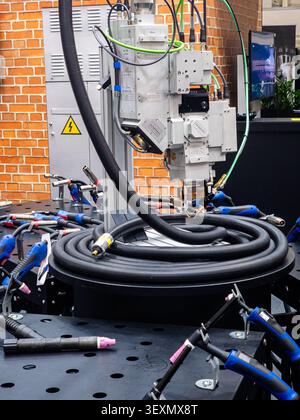 A professional, automated laser welding system head mounted over a metal workstation, surrounded by various manual MIG and TIG welding torches in an i Stock Photo