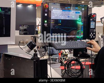 Close-up of an operator using a keyboard and mouse next to a modern CNC machine control panel with a digital screen displaying program coordinates at Stock Photo