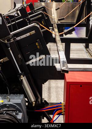 Close-up view of an automated metal tube feeding system of an industrial laser cutter, showing mechanical components, pneumatic cylinders, and a squar Stock Photo