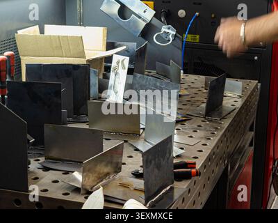 A collection of welded metal T-joint specimens arranged on a perforated welding table in an industrial workshop or training facility. Stock Photo