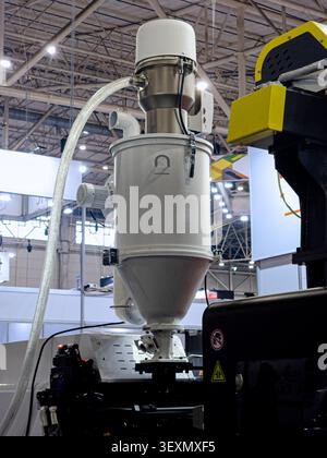 An automatic vacuum loader and hopper dryer system installed on a modern plastic injection molding machine, demonstrating automated polymer pellet han Stock Photo