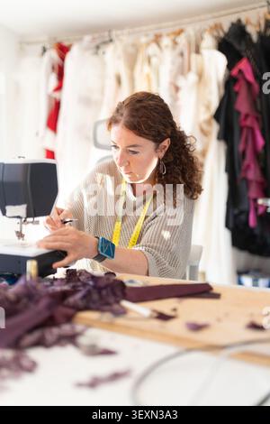Sewing in a workshop with fabrics scattered around while working on a garment design in the afternoon light Stock Photo