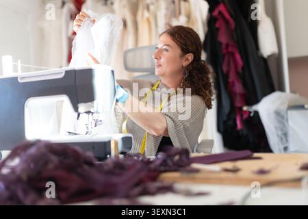 Woman sewing fabric in workshop while creating garments for upcoming fashion show in afternoon light Stock Photo