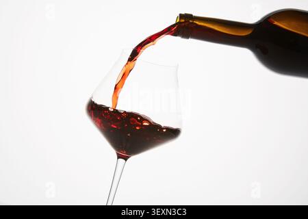 Red wine pouring into tilted wineglass from bottle. Stock Photo