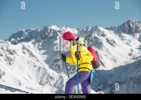 Woman Engaged in Winter Hiking With Trekking Poles Amidst Snow-Covered Mountain Range Stock Photo