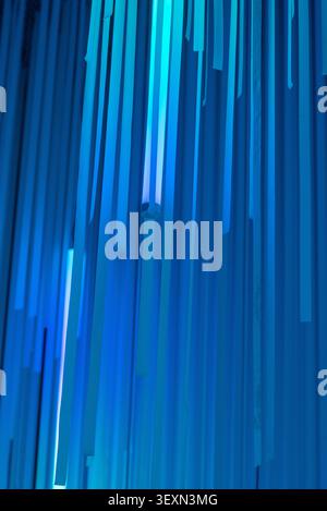 Vertical shot of an abstract geometric pattern with blue vertical panels illuminated by bright neon light tubes. Stock Photo
