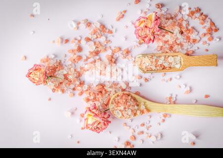 Himalayan pink bath salt with dried rose buds and wooden spoons on soft pastel background, romantic spa wellness flat lay for natural self care and be Stock Photo