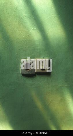 An old wall electrical power outlet paired with a light switch on a green textured concrete wall, decorated with cinematic sunlight and tree branch sh Stock Photo