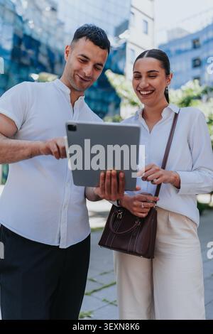 Smiling business colleagues looking at a tablet together outdoors in an urban office district Stock Photo