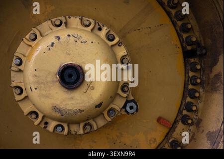 Close-up detail of a yellow industrial machine wheel and bolts, showing mechanical structure and heavy equipment design. Stock Photo