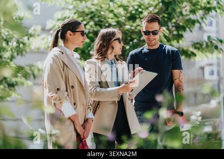 Three young professionals discussing business on a tablet during a casual outdoor meeting Stock Photo