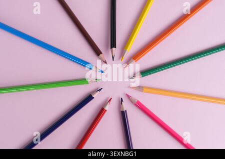 Colored pencils arranged in a circle on a pink background. Stock Photo
