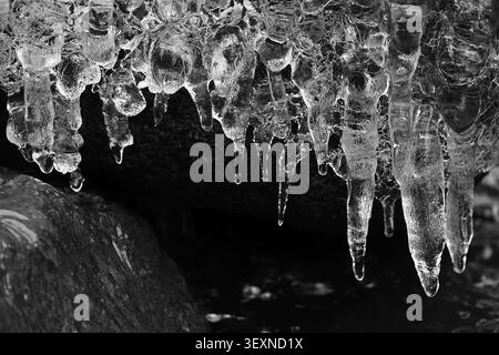 Close-up icicles dripping from rock formation in monochrome winter Stock Photo