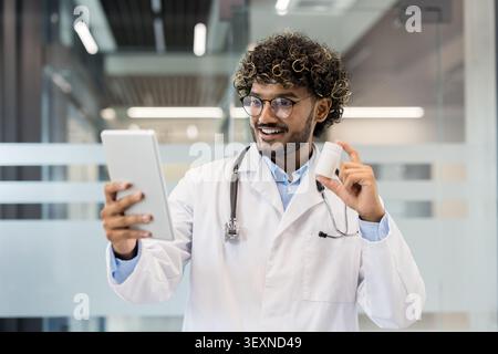 Doctor in a lab coat and stethoscope consulting a patient online, holding a bottle of pills and explaining medical information during a virtual healthcare appointment Stock Photo