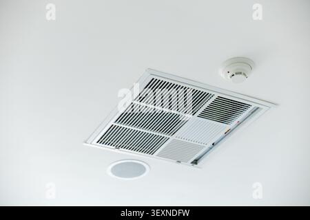 A ceiling air vent, smoke detector, and round speaker on white ceiling, modern interior safety and ventilation system, clean and minimal design Stock Photo