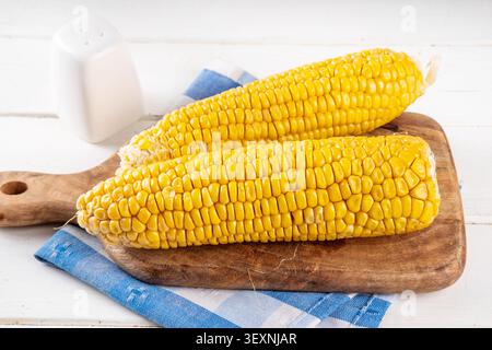 Sweet boiled corn cobs portions on plate, with salt and spices, on white wooden table copy space Stock Photo