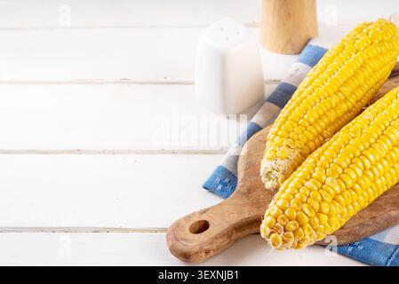 Sweet boiled corn cobs portions on plate, with salt and spices, on white wooden table copy space Stock Photo