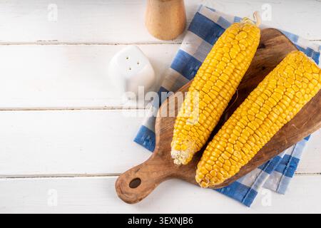 Sweet boiled corn cobs portions on plate, with salt and spices, on white wooden table copy space Stock Photo
