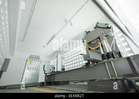 An elevator machine, steel cable, control panel, and modern equipment in bright, clean, industrial room with white walls and safety warning signs Stock Photo