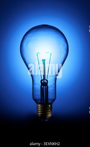 A classic incandescent light bulb glowing with a vibrant blue light against a dark background, representing creativity, intelligence, technology, and Stock Photo