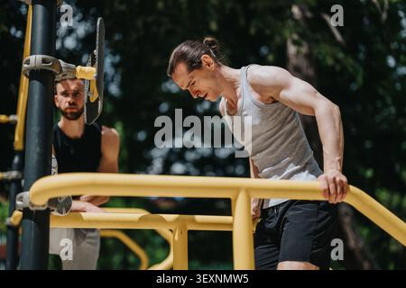 Two men doing dips on yellow parallel bars at an outdoor gym focusing on fitness and strength training Stock Photo