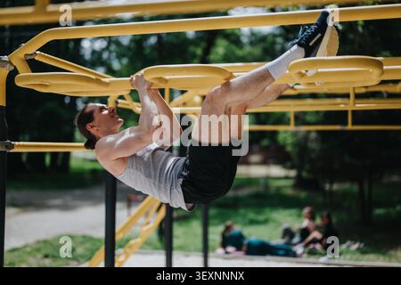 Young man doing pull-ups on yellow outdoor gym bars in park workout session Stock Photo