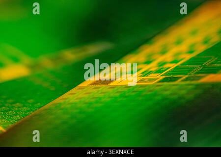 Wafer surface displaying microchip patterns, reflecting green and golden light Stock Photo