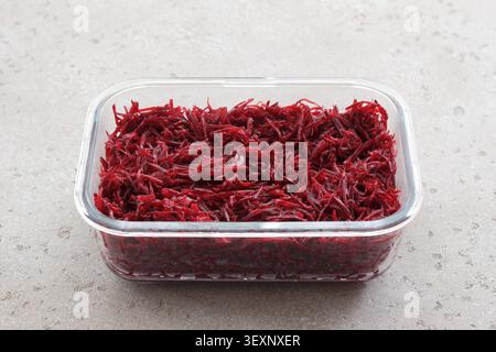 Fresh grated beetroot salad in a glass food container with fork on a light stone surface. Healthy vegetable dish, meal prep ingredient Stock Photo