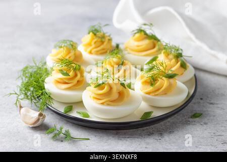 Boiled eggs stuffed with garlic and mayonnaise filling, garnished with fresh dill and green onion. Protein rich appetizer served on a plate, close up Stock Photo