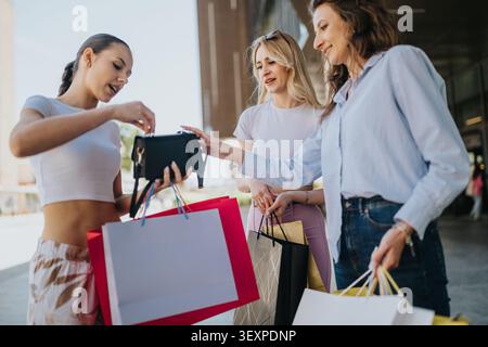 Three friends shopping together outdoors carrying colorful shopping bags and checking a small handbag Stock Photo