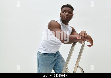 A confident African American man showcases trendy summer fashion while leaning on a ladder. Stock Photo