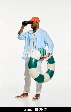 Stylish man stands near the beach holding a lifebuoy, ready for summer adventures and fun. Stock Photo