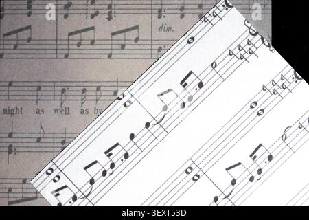 Close-up of overlapping sheet music pages featuring a modern music manuscript placed diagonally over vintage printed sheet music. Stock Photo