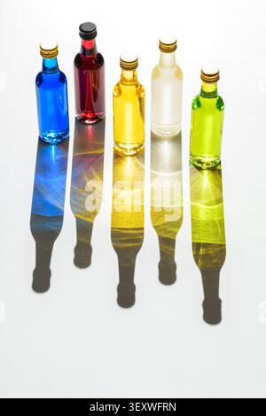 Five small glass bottles with liquids in various colors like blue. Red. Yellow. Clear. And green. Casting long. Artistic shadows with light reflection Stock Photo
