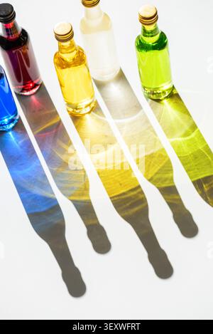 Row of small glass bottles filled with blue, red, yellow, off-white, and green liquids, creating long, vivid color and light refractions on a white su Stock Photo