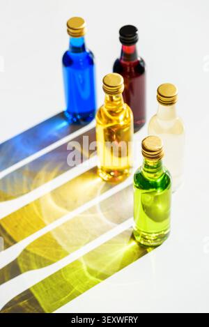 Glass mini bottles of various colors casting long, striking shadows and creating a beautiful light play on a bright surface, representing diversity an Stock Photo