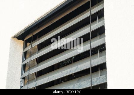 Metal window shutters angled to allow airflow while maintaining security in a residential setting. The surface shows signs of weathering with grime accumulation visible on the slats.  Stock Photo