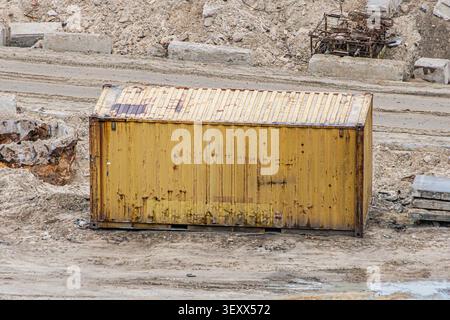Shipping container, weathered and rusted, positioned on a construction site with dirt ground and debris, including concrete blocks and twisted metal, Stock Photo