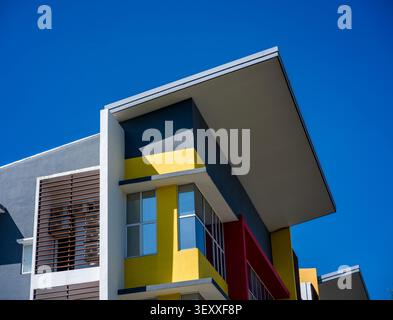 Low-angle shot of a modern building facade featuring sharp geometric lines, bright yellow and red accents, and an overhanging roof under a vibrant blu Stock Photo