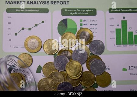 Coins are scattered on a market analysis report showing graphs and statistics. Data includes growth and consumer demographics for various regions and Stock Photo