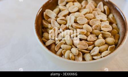 A close-up shot of a ceramic bowl filled with salted roasted peeled peanuts. Stock Photo