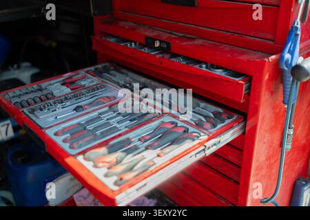 Heavy duty red metal tool chest with open drawers displaying an organized selection of screwdrivers, sockets, and hardware wrenches Stock Photo