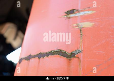 Deep scratches, peeling paint, and corrosion rust lines on the orange metal surface of industrial heavy machinery Stock Photo