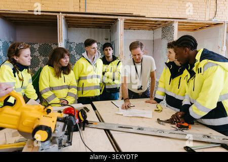 Male instructor teaching construction work to young students at vocational workshop Stock Photo